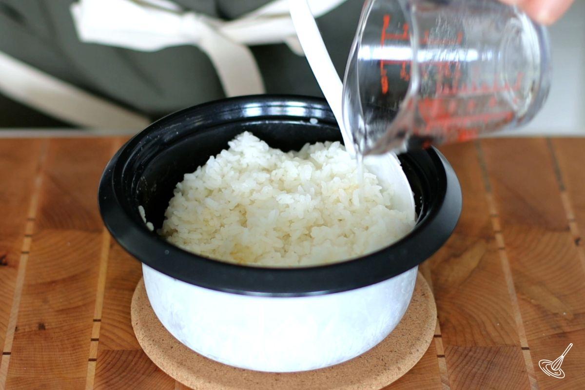 Someone pouring vinegar in a pot of cooked sushi rice.