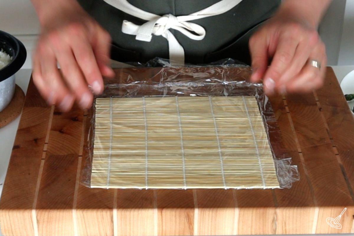 Someone wrapping a sushi mat with plastic wrap.