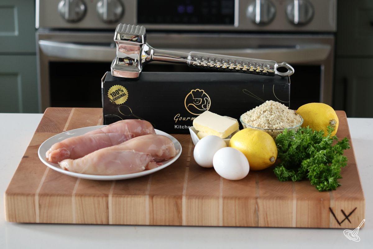Ingredients on a cutting board, including chicken breast, eggs, panko crumbs. 
