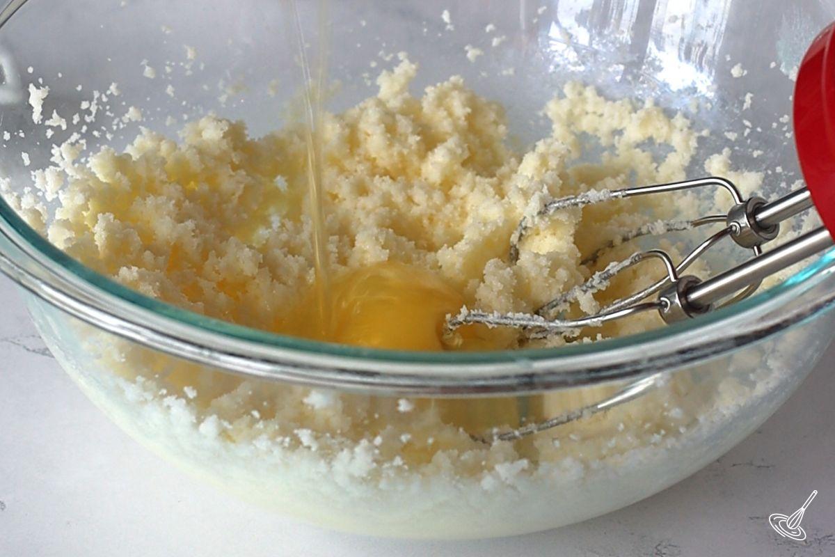 Someone adding an egg to a creamed butter and sugar mixture.