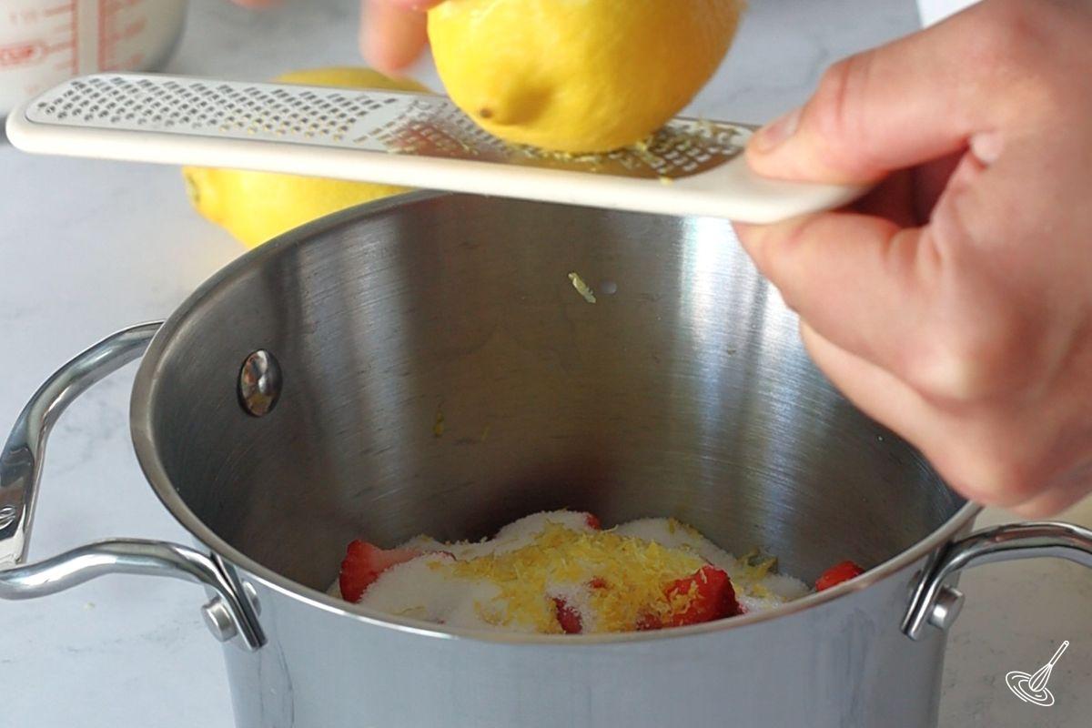 Quelqu'un qui râpe du zeste de citron dans un pot de fraises.