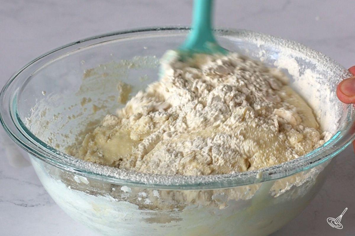 Someone using a rubber spatula to fold dry ingredients into a bowl of cake batter. 