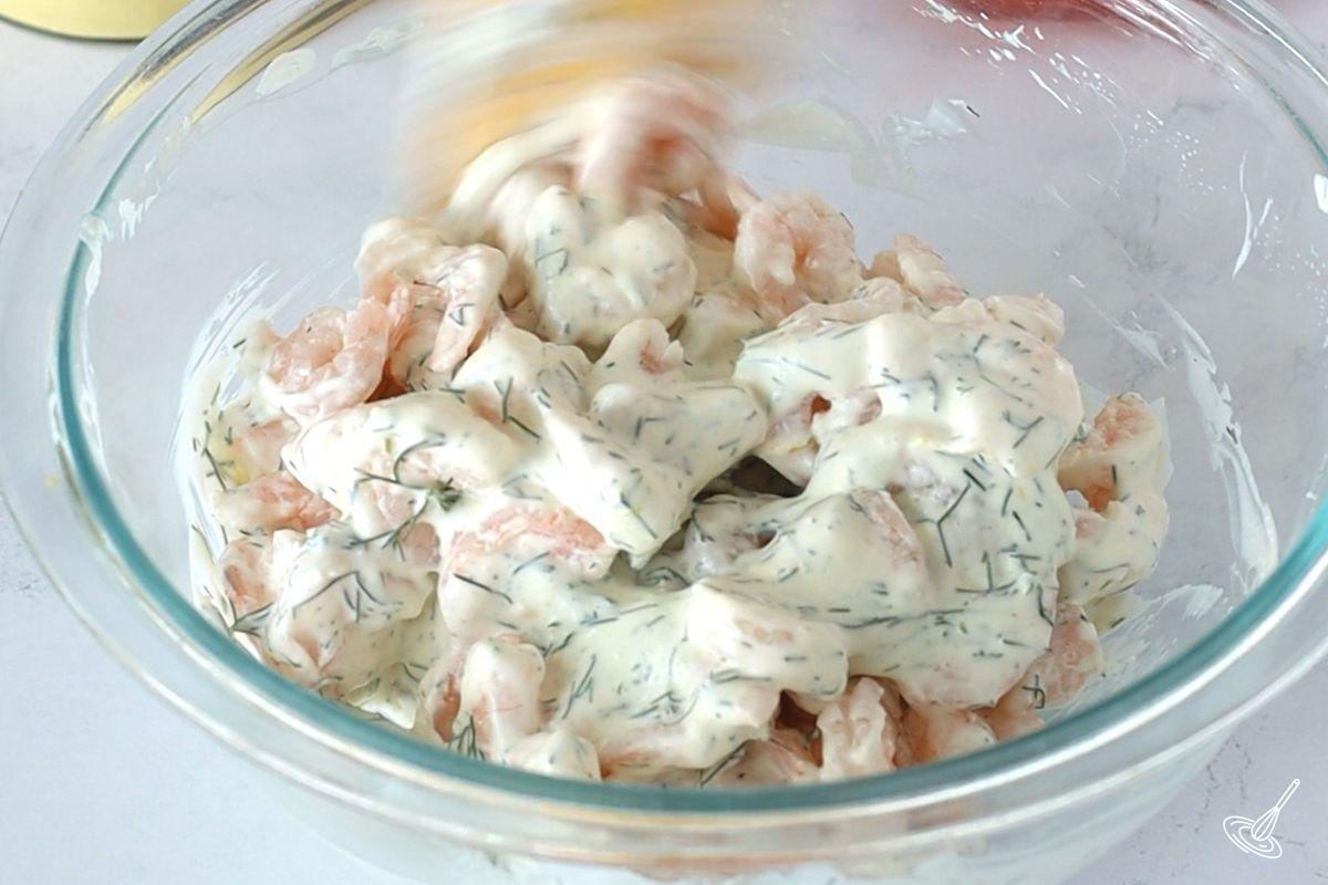 Someone stirring salad shrimp into a bowl of mayo dressing. 