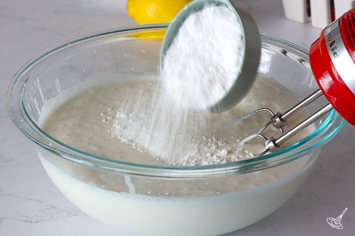 Quelqu'un qui ajoute du sucre à glacer à un grand bol de crème fouettée. 