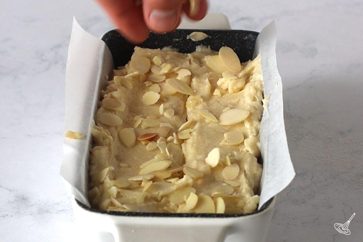 Someone sprinkling sliced almonds on top of an Almond Pound Cake before baking.