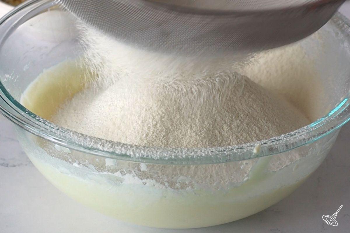 Someone sifting flour over a bowl of cake batter.