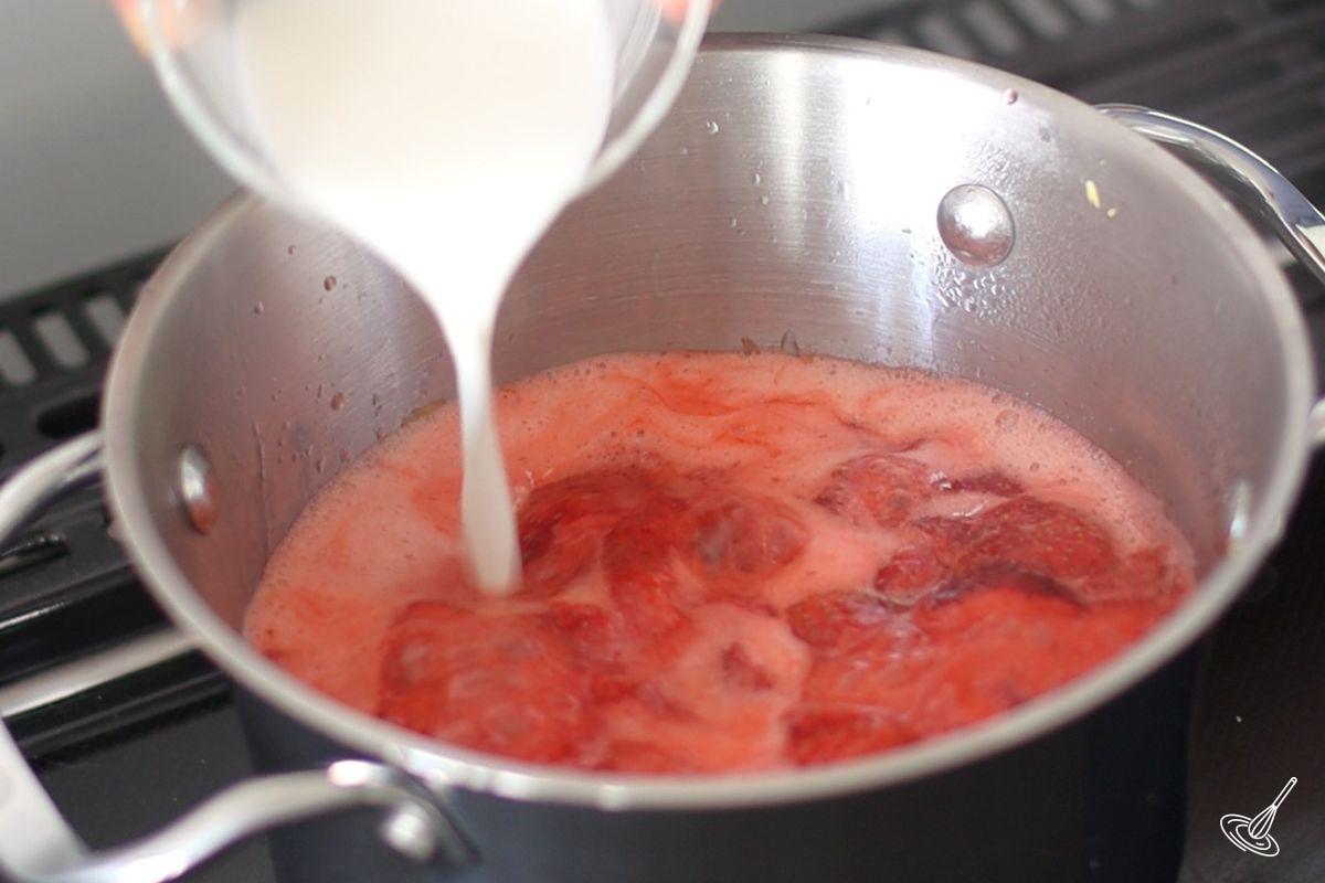 Quelqu'un verse un mélange de fécule de maïs dans une casserole de compote de fraises qui mijote.