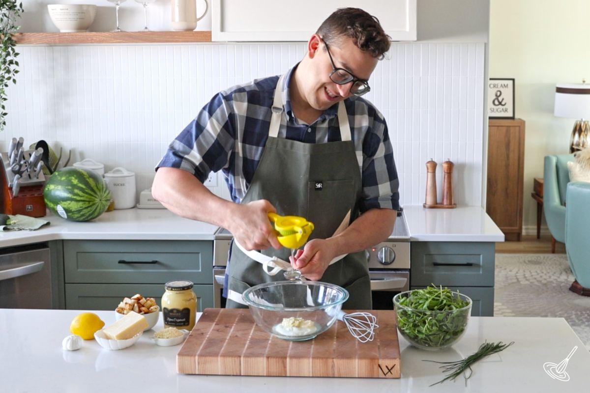 Someone squeezing the juice out of a lemon over a bowl of salad dressing.