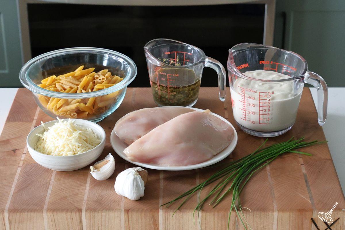 Ingredients to make chicken pesto alfredo, including chicken breast, pasta, pesto, and alfredo sauce. 