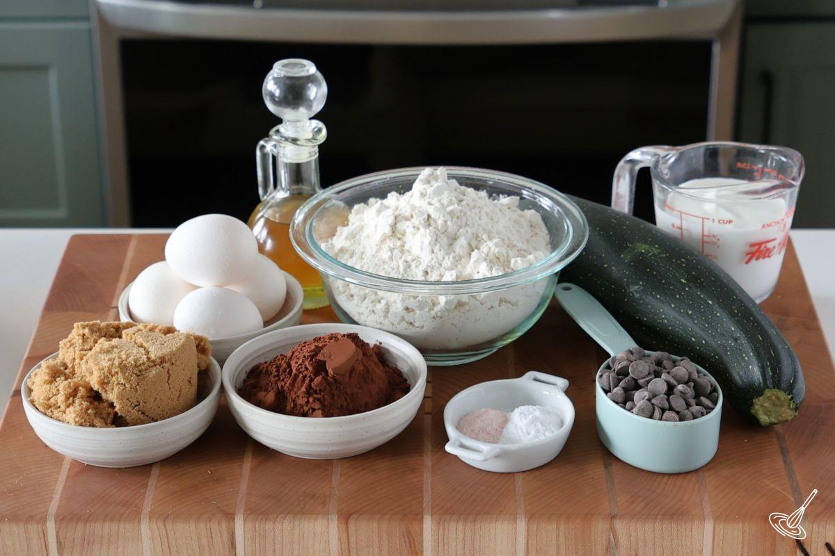 Ingredients on a cutting board to make a zucchini cake, including cocoa powder, flour, eggs, sugar, and yogurt.