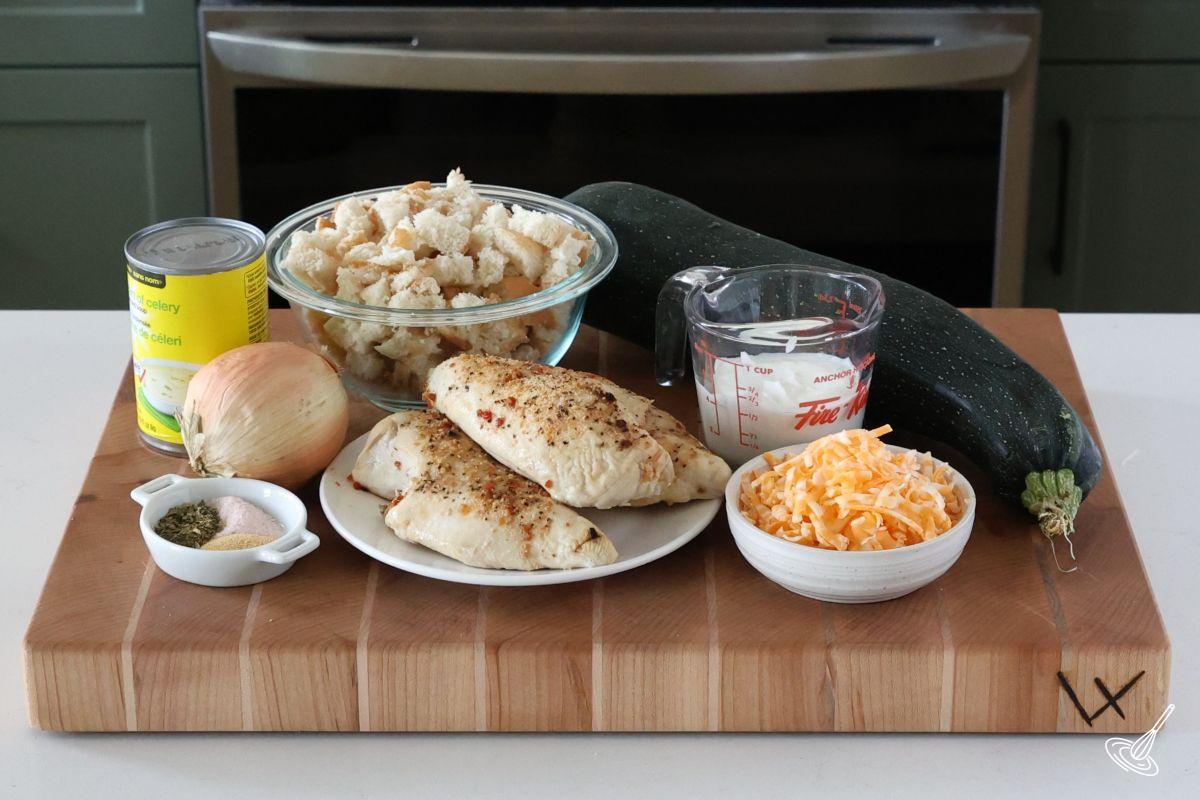 Ingredients on a cutting board, including zucchini, cooked chicken bread, cubed bread, and grated cheese.