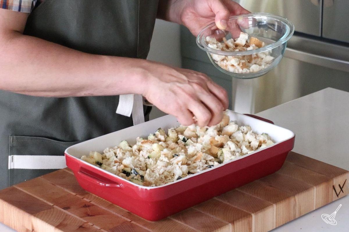 Someone adding cubed bread on top of a Chicken and Zucchini bake.