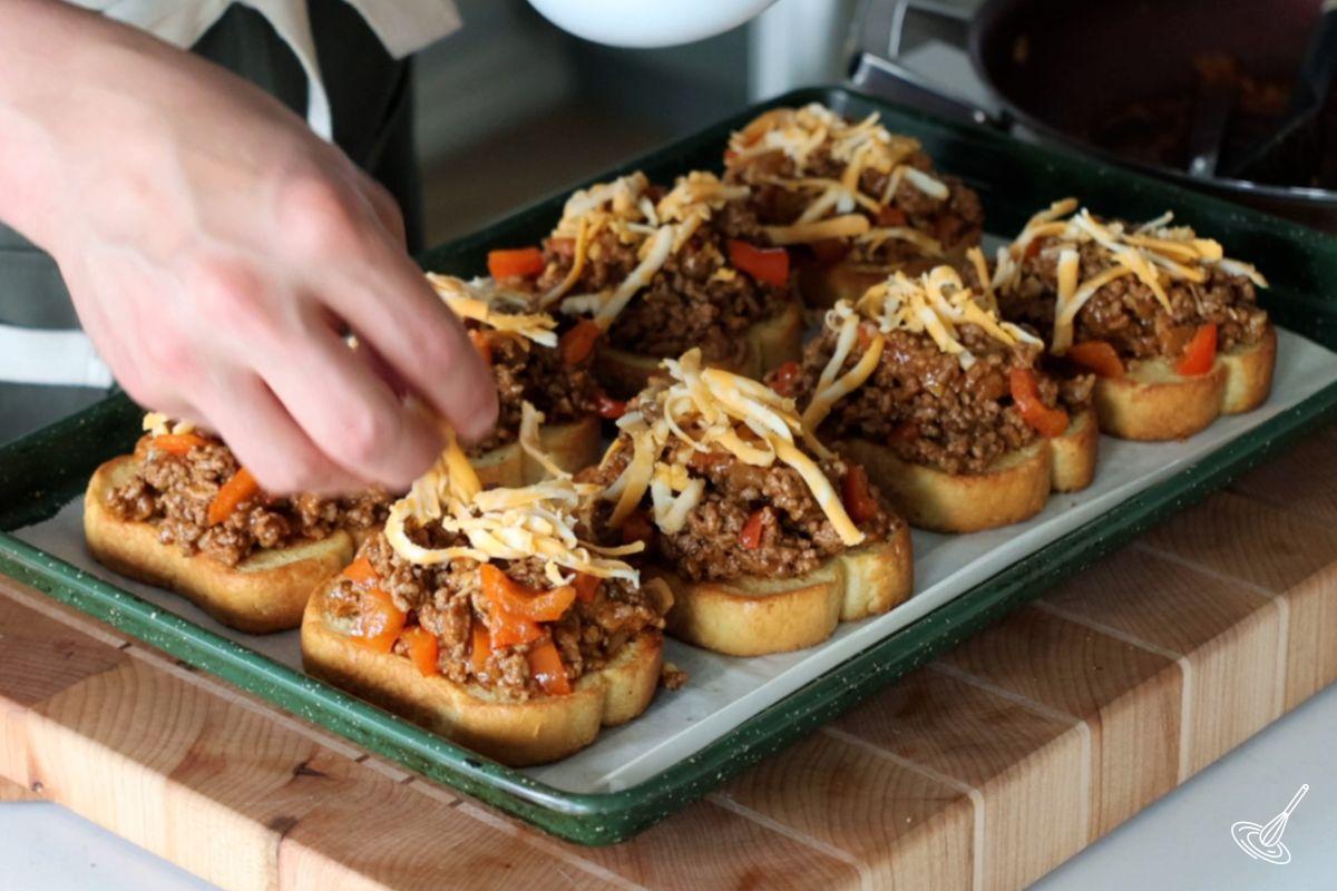 Someone sprinkling grated cheese on top of Texas Toast Sloppy Joes.