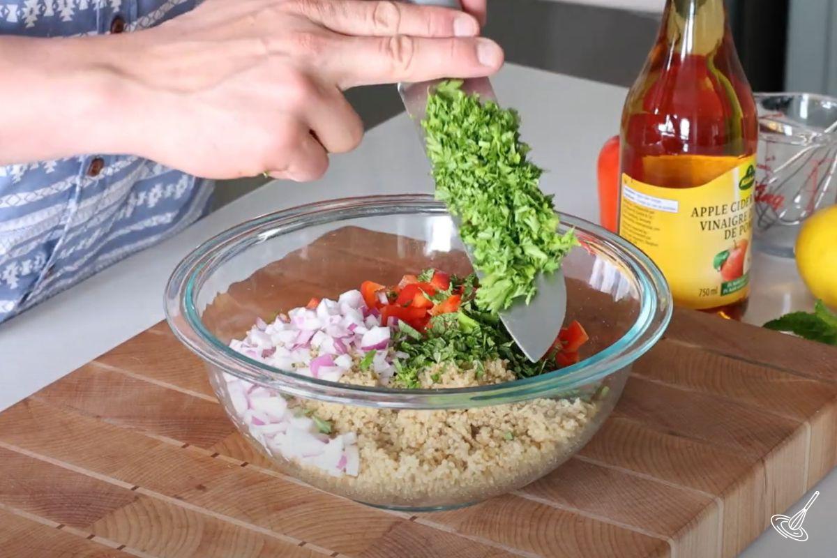 Someone adding chopped parsley to a bowl of quinoa salad.