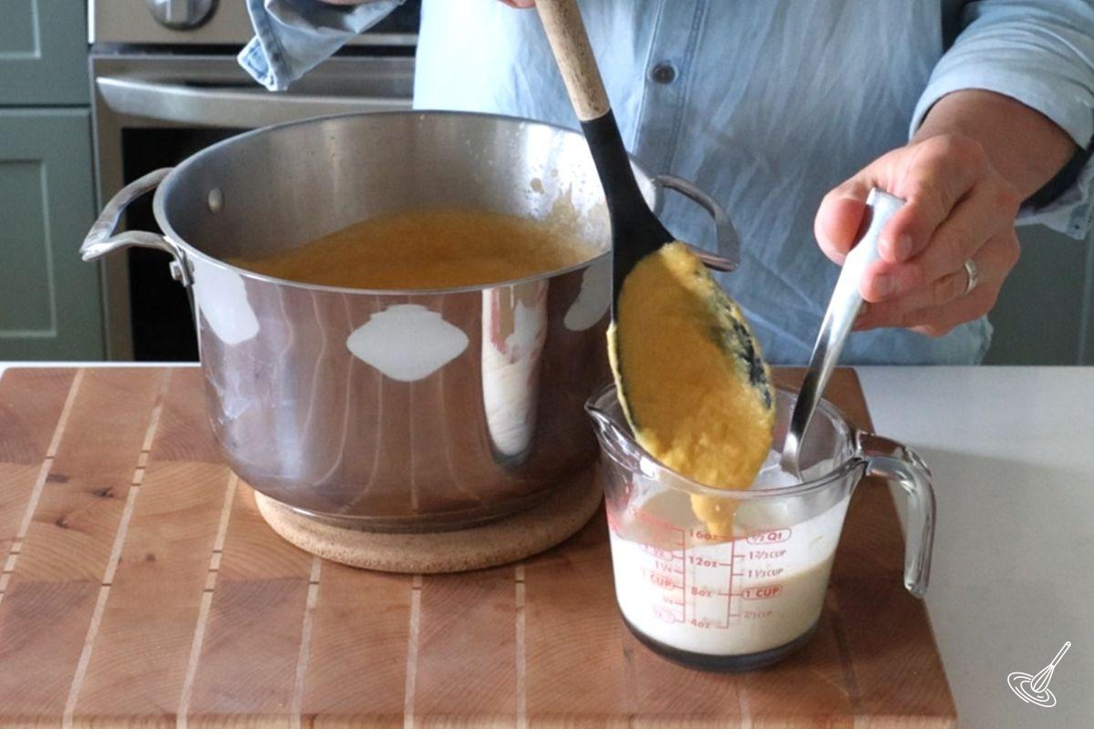Someone tempering heavy cream with a ladle of soup.
