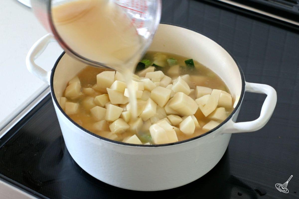 Someone pouring chicken broth into a pot of soup. 