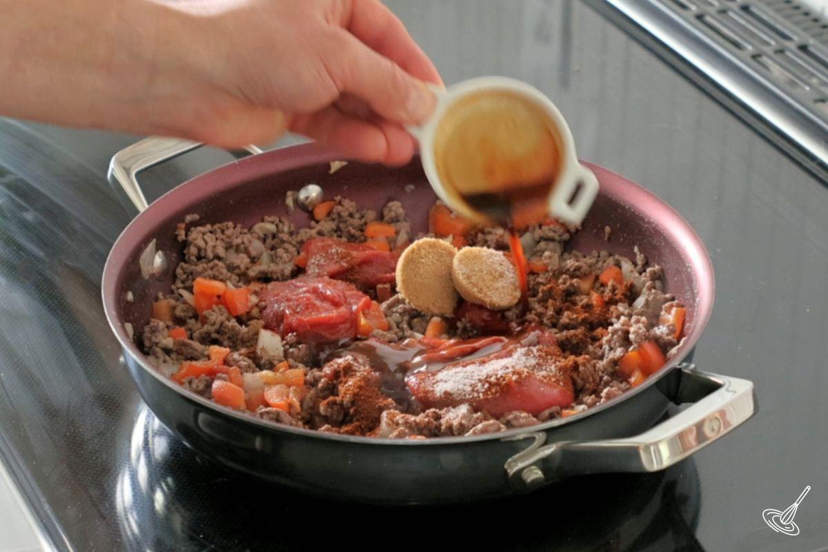 Someone adding brown sugar and hot sauce to sloppy joes mixture.