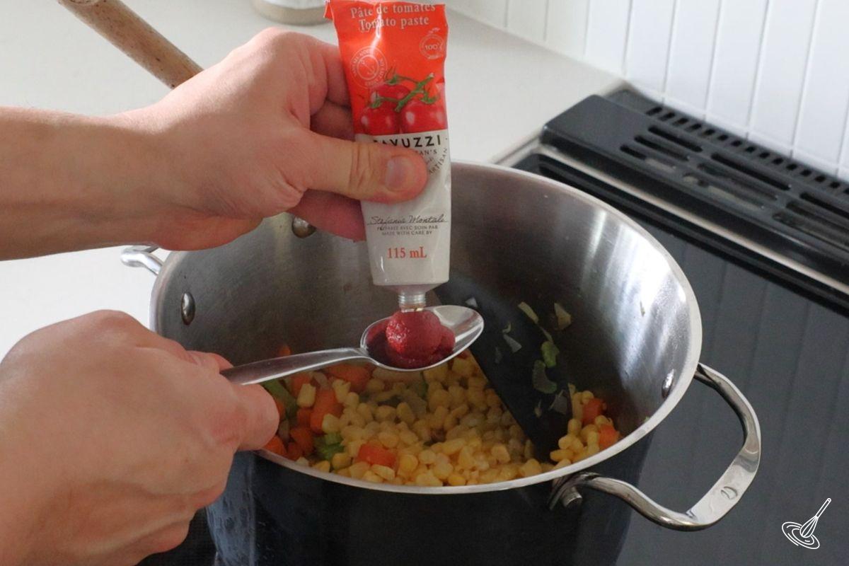 Someone squeezing out a tube of tomato paste, onto a spoon.
