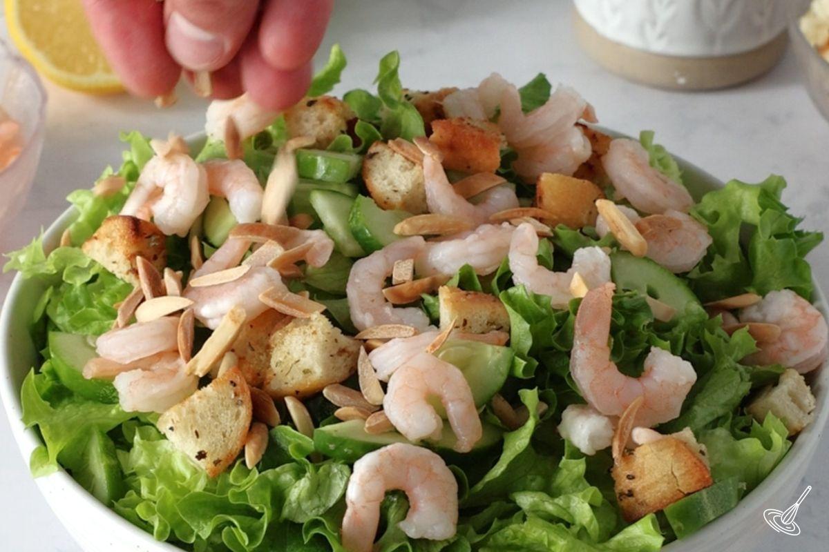 Someone adding toasted almond on top of an Apple Almond Shrimp Salad.