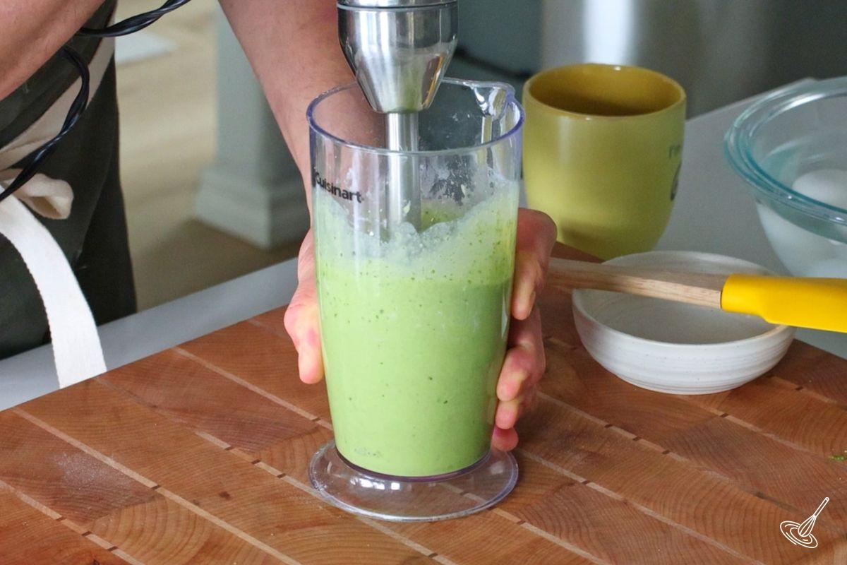 Someone using an immersion blender to blend spinach crepes batter.
