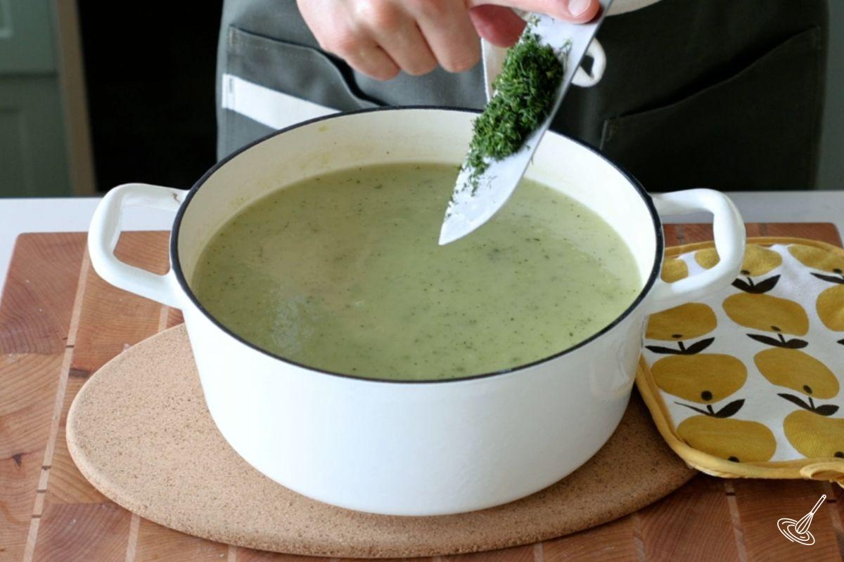 Someone adding chopped dill to a pot of zucchini dill soup. 