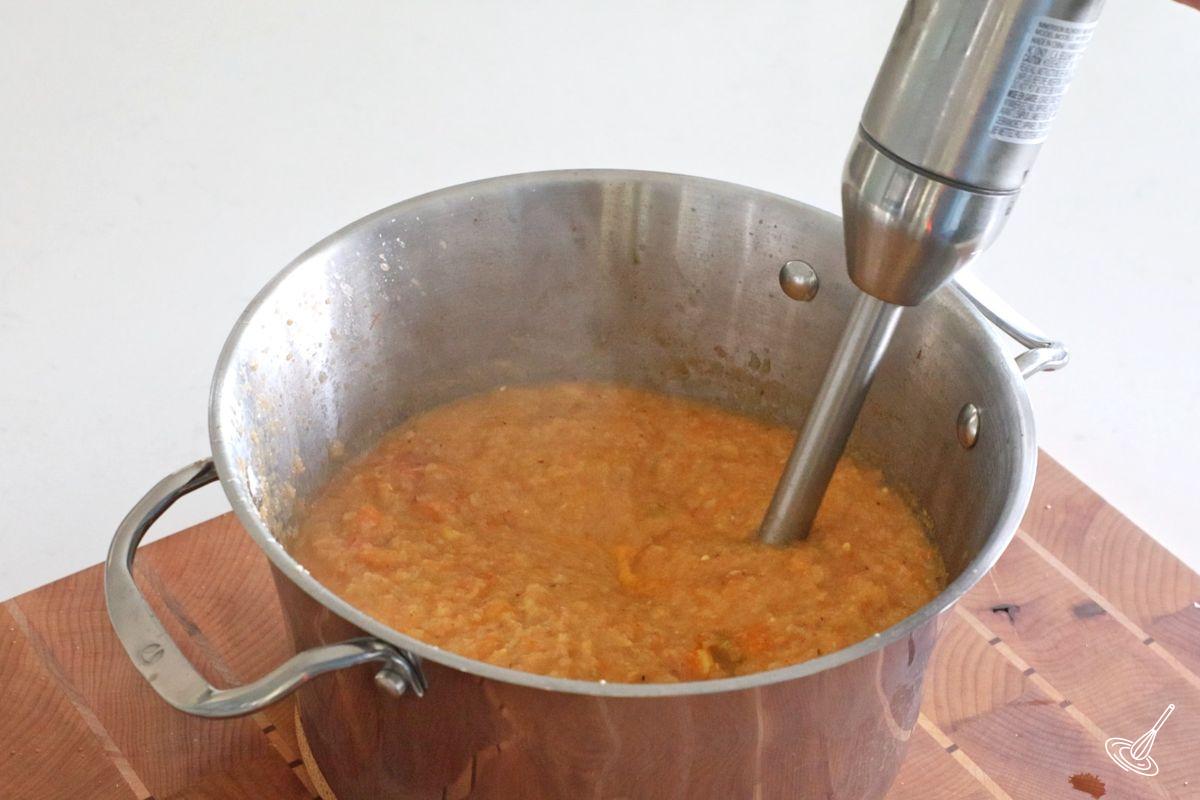 Someone using a stick blender to puree a cauliflower bisque soup. 