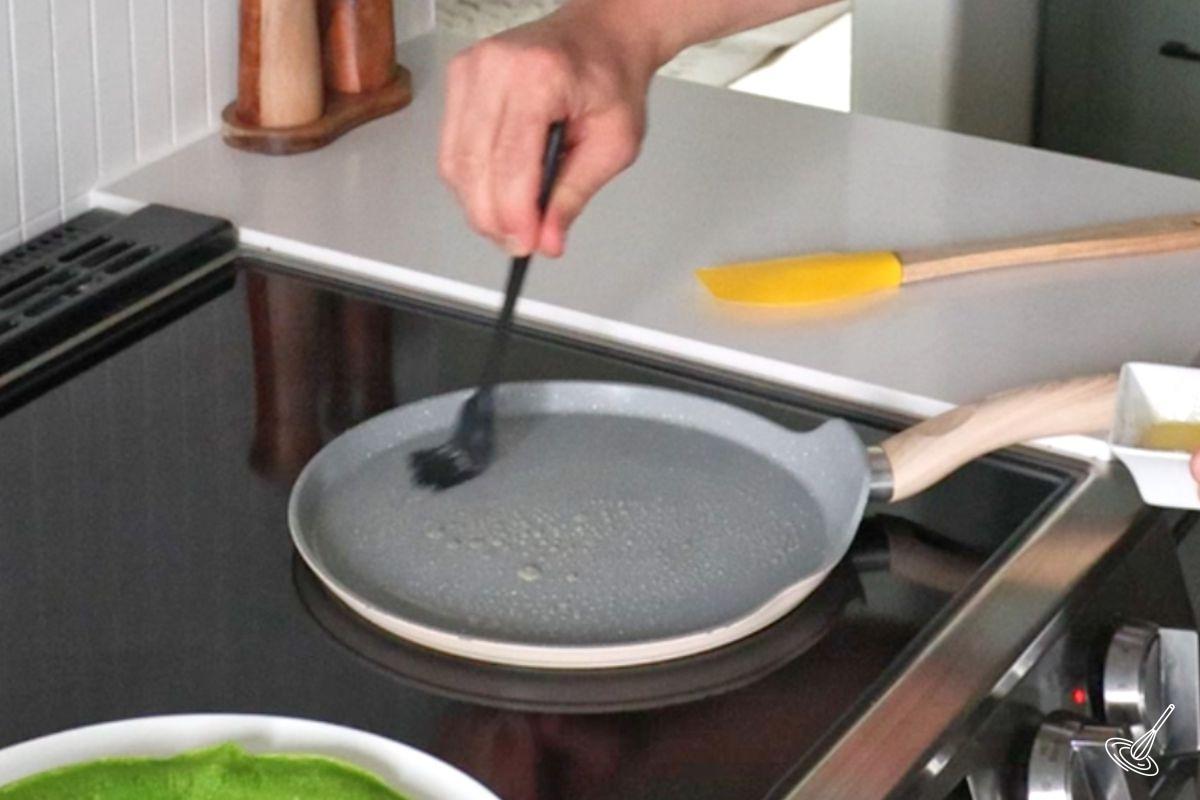 Someone brushing a crepes pan with butter.