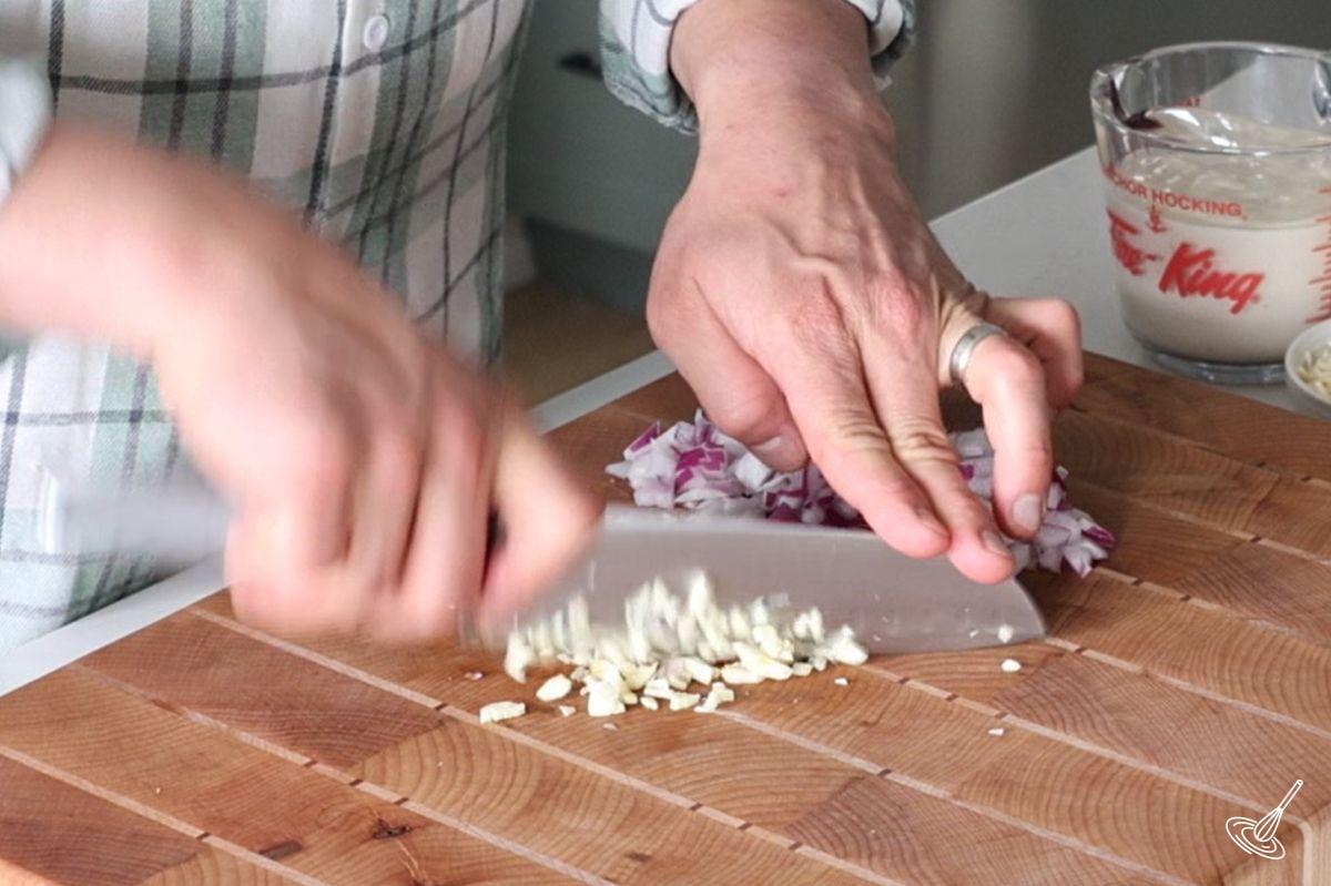 Someone mincing garlic on a wooden cutting board. 