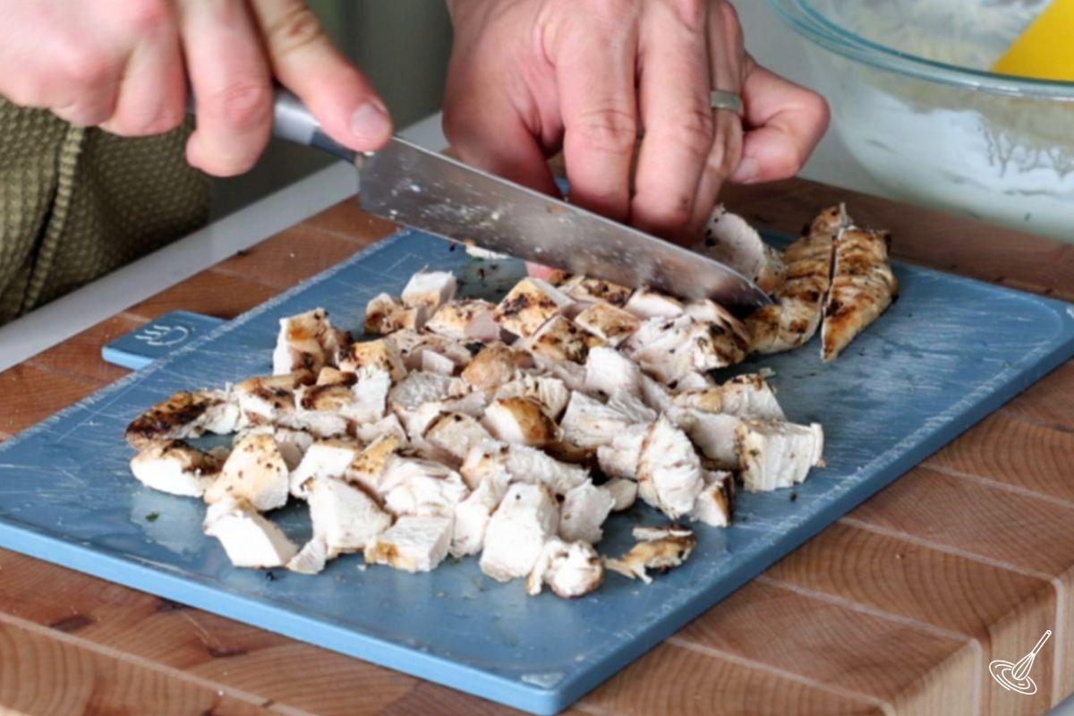 Someone cutting cooked chicken breasts into small cubes.