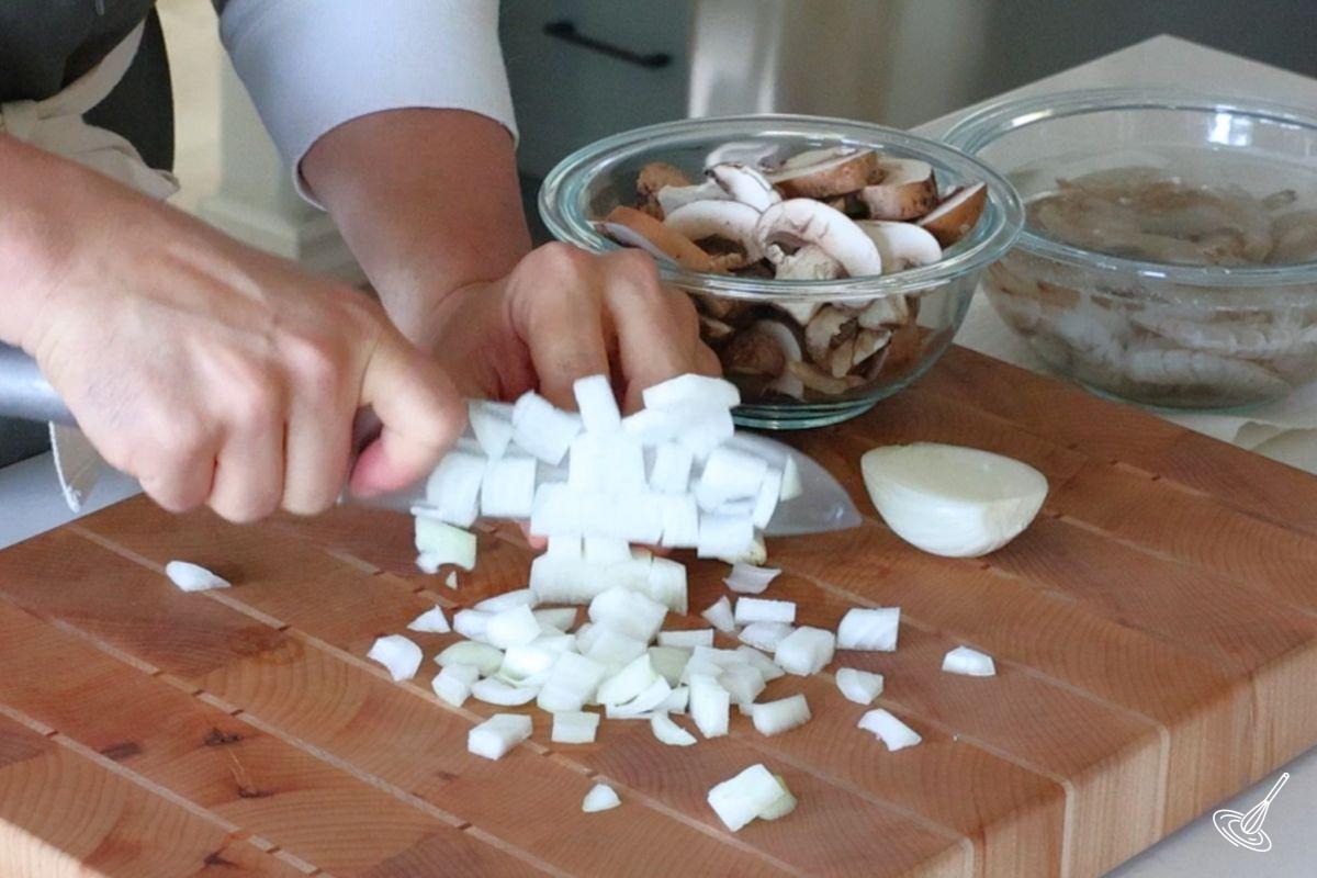 Someone chopping an onion on a wooden cutting board.