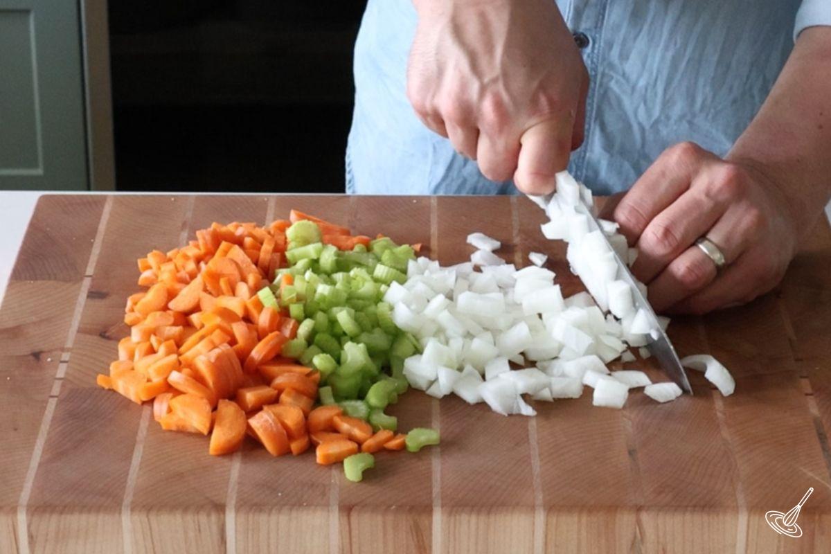 Someone chopping onion with celery and carrots. 