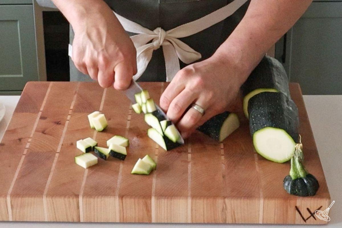 Someone cutting zucchini into small cubes. 