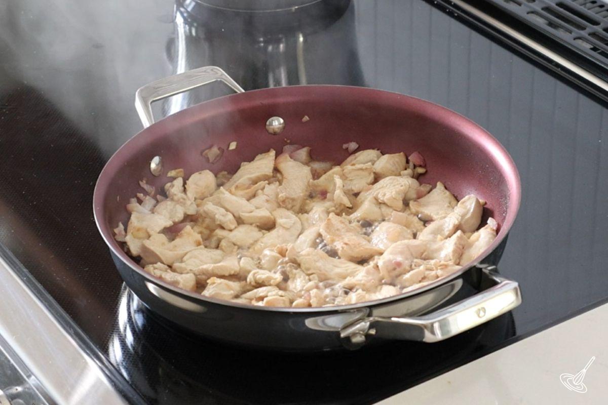 Slices of chicken cooking in a large skillet.
