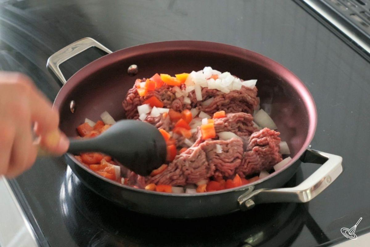 Someone cooking ground beef and vegetables in a large frying pan. 