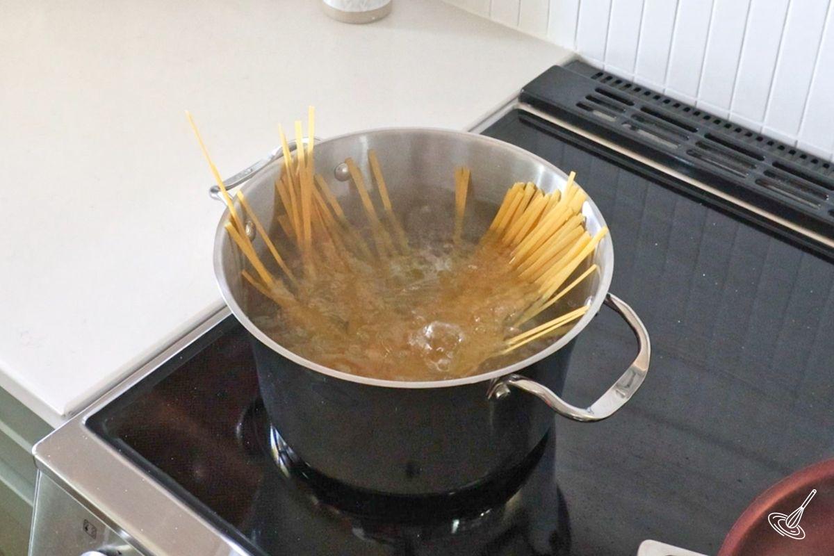 Someone cooking long pasta in a pot of boiling water.
