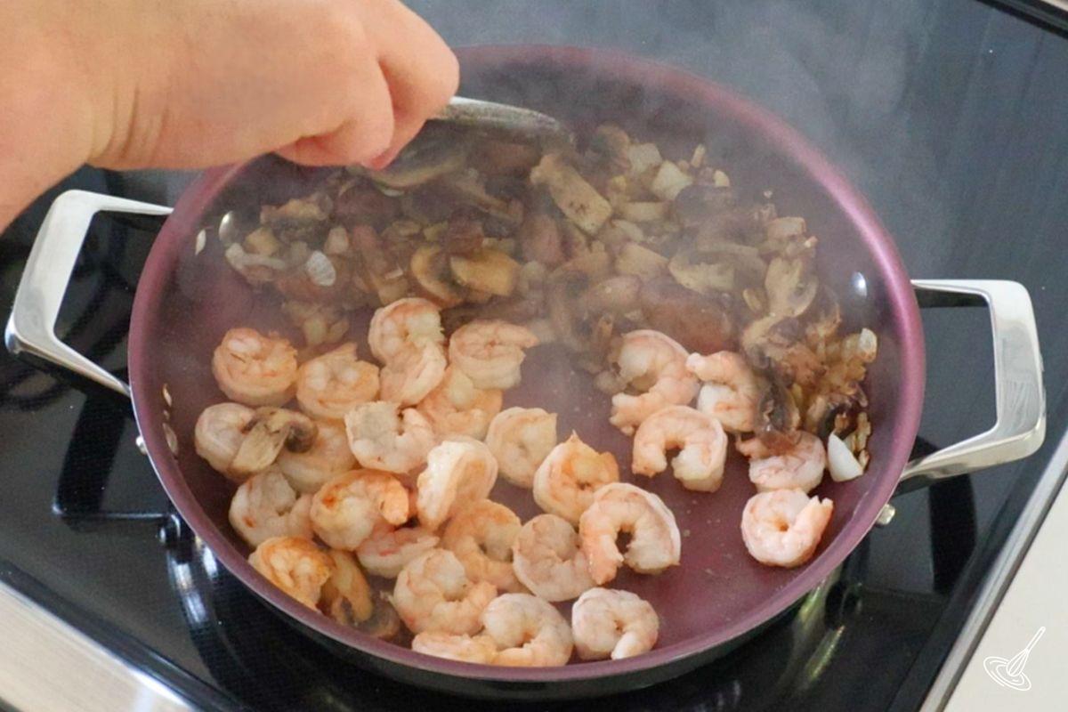 Someone cooking shrimp in a frying pan with vegetables.