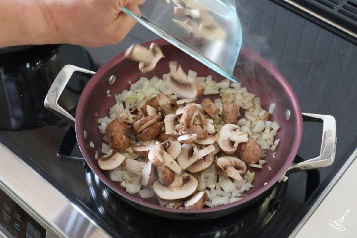 Someone cooking mushrooms onion and garlic in a large frying pan. 