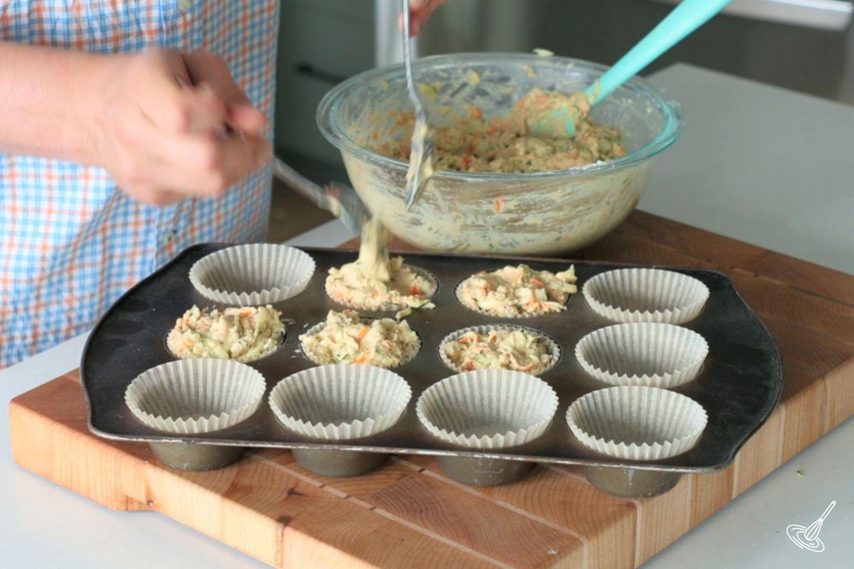 Someone scooping out carrot cake zucchini muffins batter in a muffin tin.