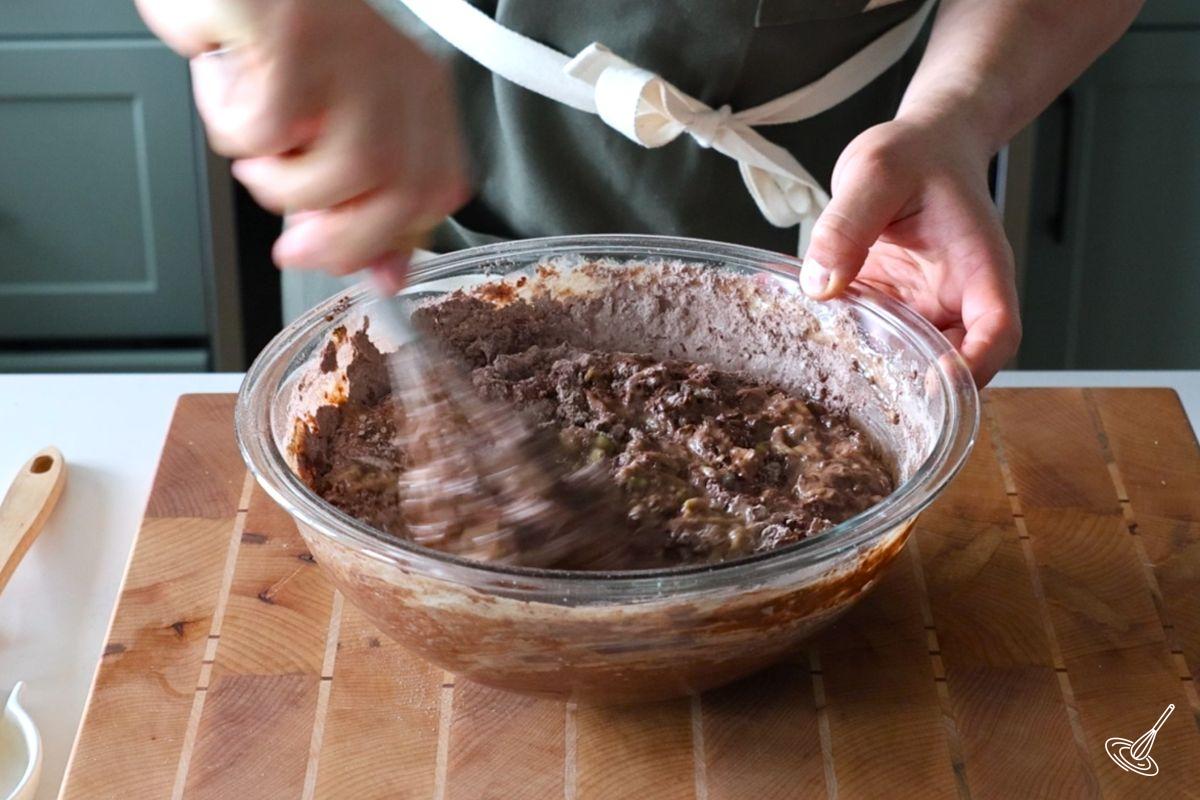 Someone mixing a large bowl of chocolate zucchini cake batter.