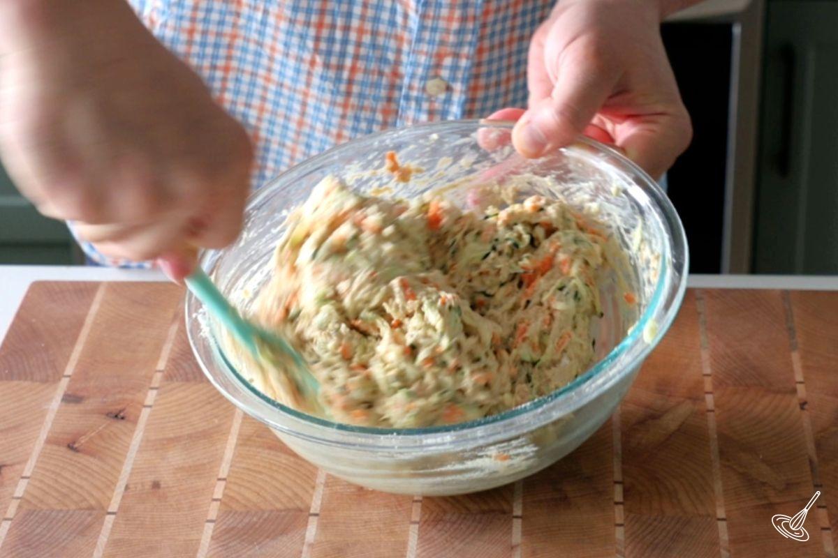 Someone folding in zucchini and carrot into muffin batter.