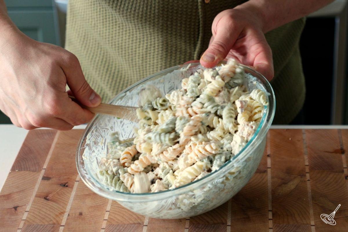 Someone using a spatula to mix together a Chicken Caesar Pasta Salad Without Lettuce.