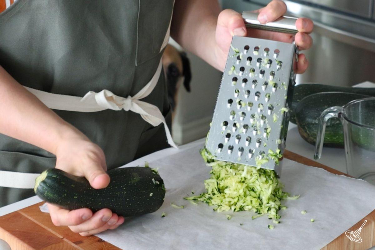 Someone using a cheese grater to grate a zucchini.