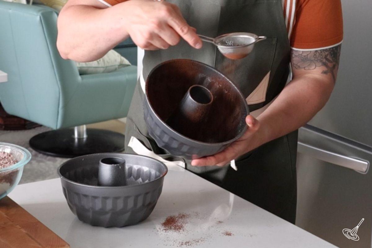 Someone using a small sifter to dust cocoa powder into bundt cake molds.