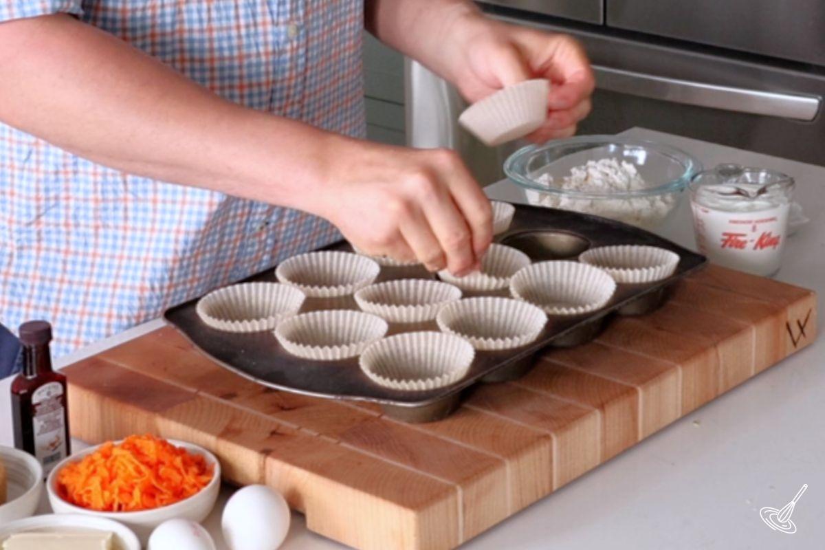 Someone placing paper liners in a muffin tray. 