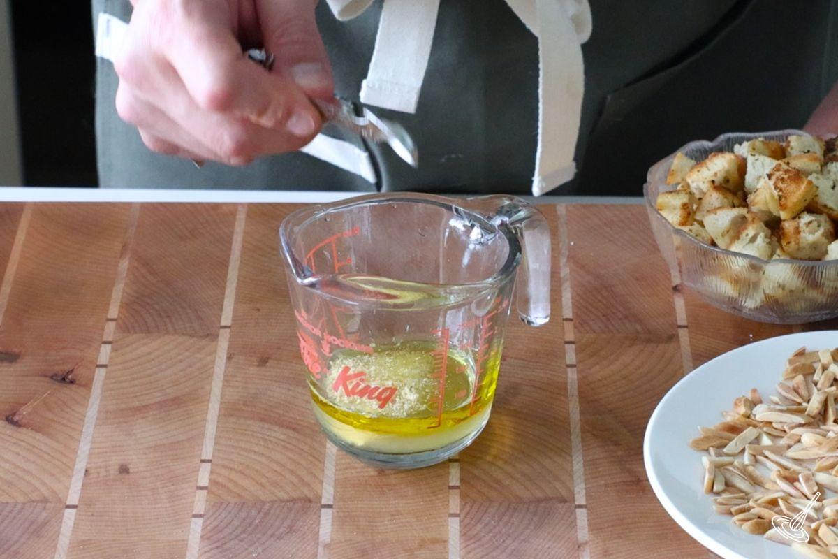 Someone adding seasoning to a measuring cup of salad dressing. 