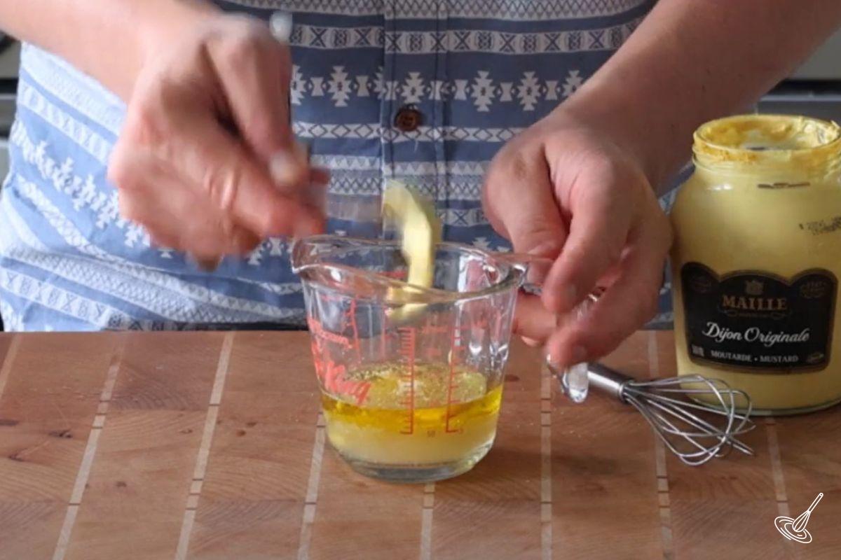 Someone adding mustard to a salad dressing. 