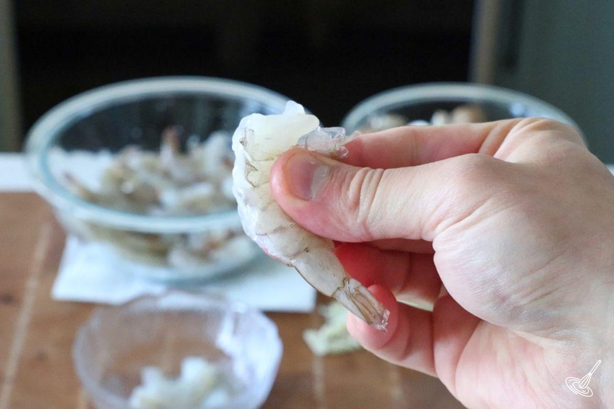Someone using their hand to peel a shrimp. 