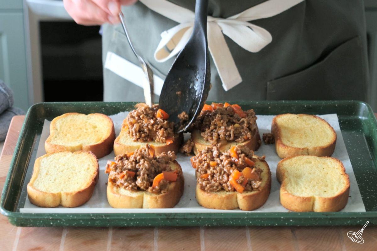 Someone placing sloppy joes mixture on top of Texas Toast.
