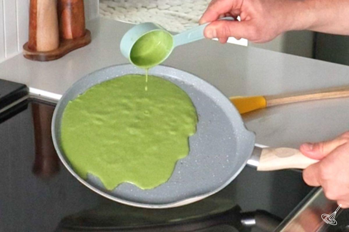 Someone pouring spinach crepes batter over a crepes pan.