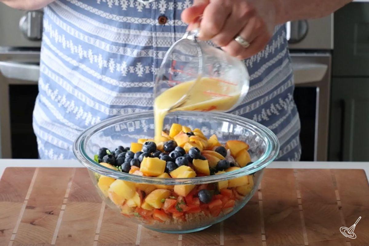 Someone adding salad dressing to a peach quinoa salad. 